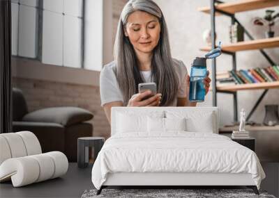 Active middle-aged caucasian woman using smart phone while training at home Wall mural