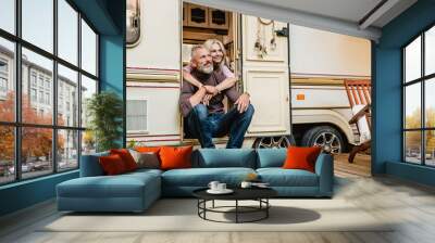 Aged happy couple sitting in the van doorway and hugging with love Wall mural