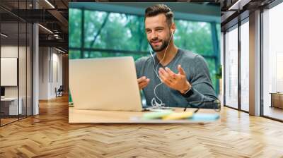 Attractive 30s caucasian businessman having online conversation using laptop and headphones at office desk Wall mural