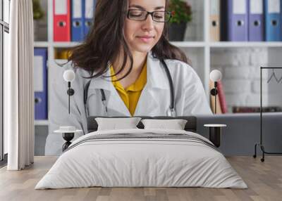 Attractive female doctor working on her laptop in hospital office Wall mural