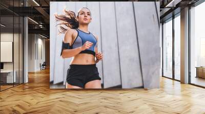 Attractive female jogger running near the grey wall listening to the music Wall mural