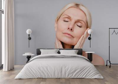 Beautiful aged white woman touching her clean pure face with her eyes closed isolated over grey background Wall mural