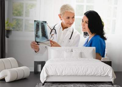 Caucasian senior female doctor showing x-ray image of lungs to medical student intern nurse caregiver, explaining disease illness diagnosis Wall mural