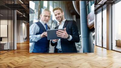 Cheerful young businessman with digital tablet discussing with senior male colleague in office lobby Wall mural