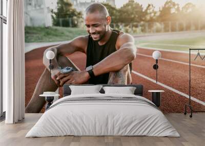 Cheerful young sporty man sitting on stadium running track with bottle of water in hands Wall mural