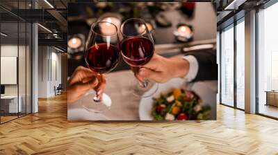 Close up of young couple toasting with glasses of red wine at restaurant Wall mural