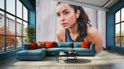 Close up shot of young pretty caucasian female athlete resting after jogging with earbuds against grey wall Wall mural