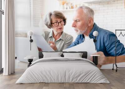 Concentrated concerned european senior old elderly couple spouses grandparents doing paperwork, paying domestic bills, rentals, receiving pension, calculating funds and budget at home kitchen Wall mural