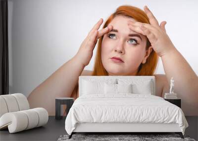 Corpulent cute redhead woman looking at her face for skin problems isolated over white background Wall mural