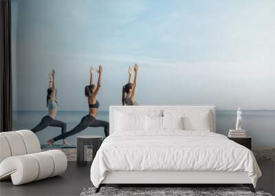 Full length image of young multiethnic group of woman practicing yoga exercise at the beach near water Wall mural