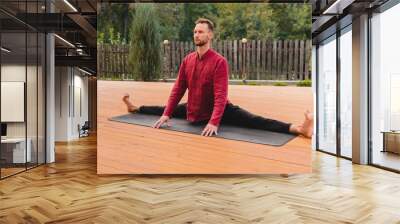 Handsome caucasian adult male yogi sitiing in full split outdoors Wall mural