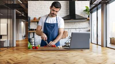 Handsome caucasian man cooking on kitchen with laptop on table Wall mural