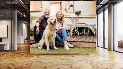 Happy aged european couple resting in the yard with their dog with motorhome in the background Wall mural