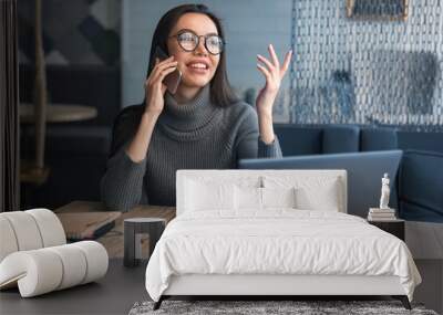 Happy business woman talking on cell phone sitting at table and working. Asian female sitting at office having telephonic conversation with client and smiling with look away Wall mural