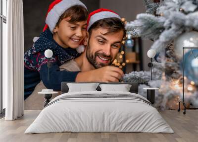 Happy father and his little son having fun while decorating the Christmas tree at home Wall mural