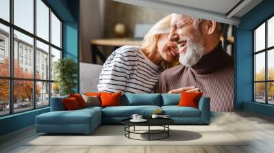 Happy laughing middle aged couple bonding while relaxing sitting on sofa Wall mural