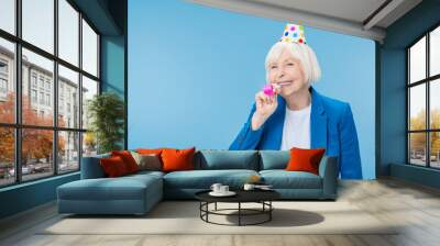 Happy mature woman in party hat making noise isolated on blue background Wall mural