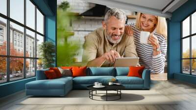 Happy senior couple using digital tablet in kitchen at home Wall mural