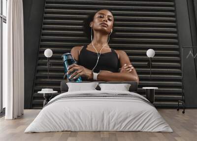 Low angle shot of african american woman in fitness sportswear taking a break from excercises standing with a water bottle in hand Wall mural