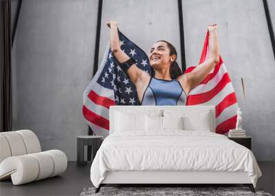 Low angle view photo of 20s happy female athlete holding American flag against grey wall Wall mural