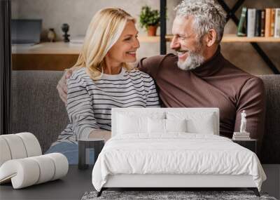 Middle aged couple relaxing and hugging on sofa at home with look on each other Wall mural