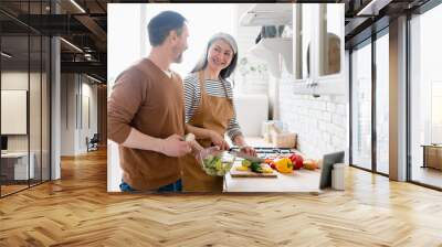 Middle-aged mature happy family couple wife and husband cooking vegetable salad together in the kitchen, helping with preparing food meal. Togetherness and vegetarian lifestyle. Wall mural