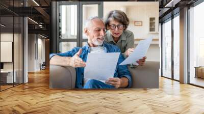 Mortgage loan debt transactions paying bills and documents. Caucasian senior old couple spouses reading marriage contract, doing paperwork, dealing with data at home Wall mural