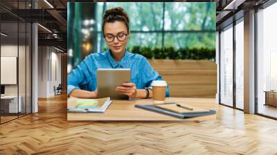 Nice-looking young caucasian businesswoman using tablet at the desk in modern office Wall mural