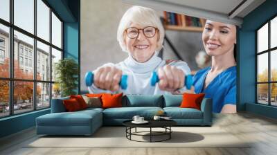 Old woman training with physiotherapist using dumbbells at home Wall mural