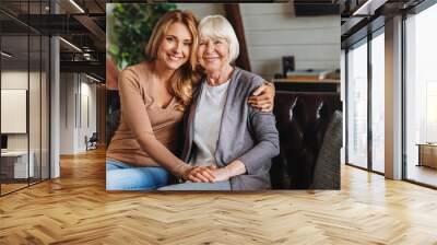 Portrait of elderly mother and middle aged daughter smiling together on the couch at home Wall mural