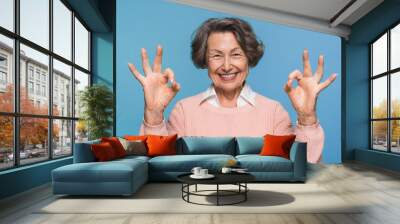 Portrait of positive smiling mature woman showing two ok okay sign gesture headshot at studio. Elderly lady giving good advice, offer, help looking at camera portrait isolated on blue background. Wall mural