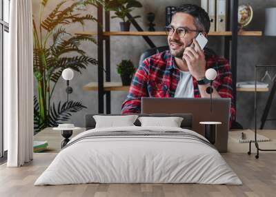 Portrait of smiling grey hair man with beard sitting front table with laptop, talking on phone Wall mural