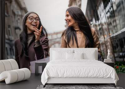 Portrait of two happy women with shopping bags pointing while walking together on the city streets Wall mural