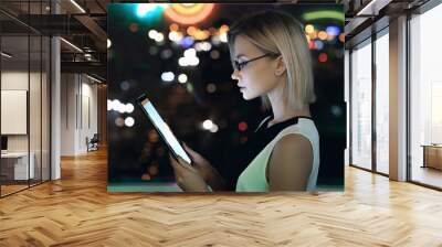 Side view horizontal shot of attractive female businesswoman ceo entrepreneur student in glasses that reading watching checking message news task late night in office building standing against window Wall mural