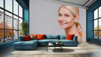 Side view portrait of good-looking mature blonde woman with clean skin smiling isolated over grey background Wall mural