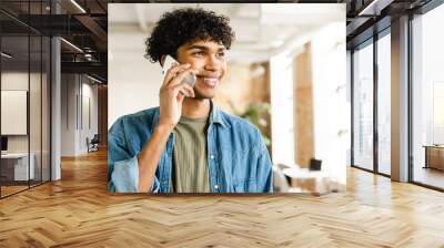 Smart afro mixed-race young business man guy freelancer student manager talking on mobile phone with customers partners colleague while working in the office coworking Wall mural