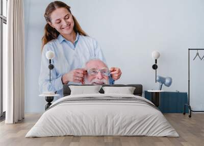 Smiling female oculist helping her mature male patient choose glasses Wall mural