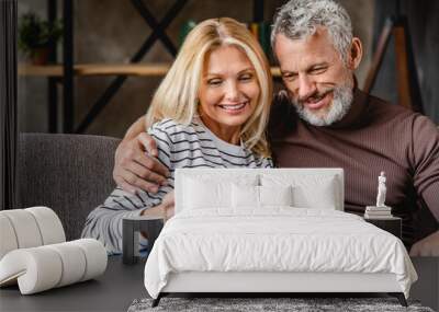 Smiling middle aged couple using digital tablet on sofa at home Wall mural