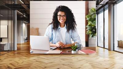 Successful young afro businesswoman working at her office desk. Front view of smiling african american female freelancer working at home Wall mural