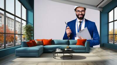 Successful young Arab engineer with clipboard and hardhat isolated over grey background Wall mural