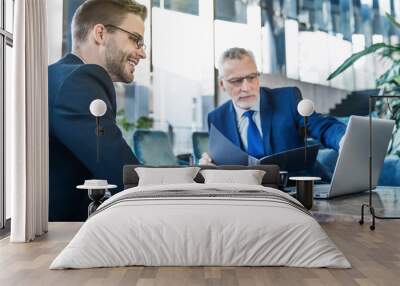 Two businessmen using laptop in lobby of modern office Wall mural