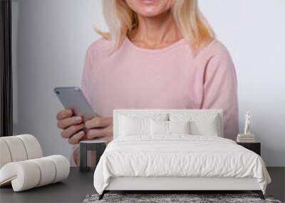 Vertical photo of middle-aged caucasian woman using smart phone in casual attire isolated over grey background Wall mural