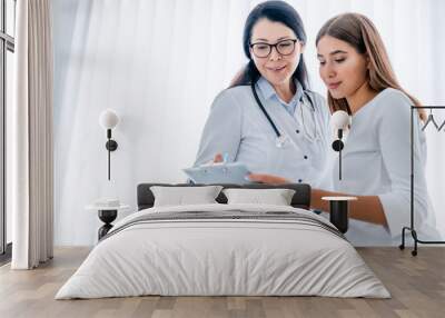 Woman doctor and her patient looking at tablet together and discussing Wall mural