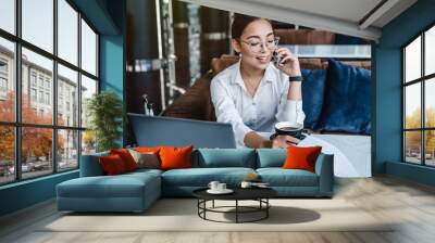 Woman entrepreneur managing her business from office lobby working on laptop computer and discussing business using smartphone Wall mural