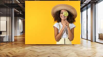 Young african girl kid in hat with candy isolated over yellow background Wall mural