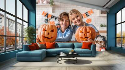 Young boy brother son kid and sister daughter girl child having fun with pumpkins on Halloween at home kitchen. Kids children making cutting decorating orange pumpkins. Spooky autumn season concept Wall mural