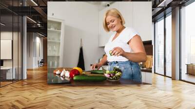 Young caucasian plump plus size woman cooking making salad, healthy food, dieting, counting calories, preparing dinner lunch at home kitchen Wall mural