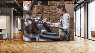 Young caucasian woman in apron working with cash box in coffee shop behind the counter. Female worker, barista, waitress, manager, administrator checking bill order on digital cash register. Wall mural