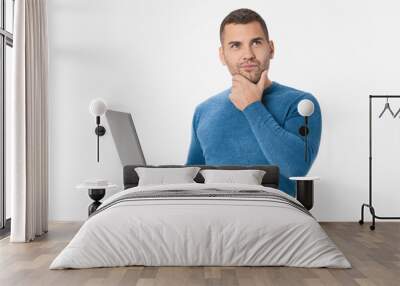 Young thinking man holding laptop isolated over white background Wall mural