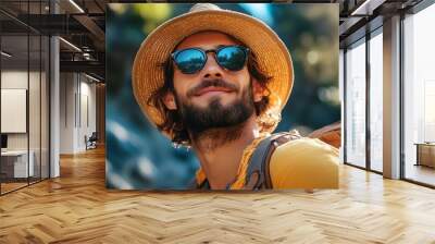 A man wearing a straw hat and sunglasses is smiling and posing for a picture. He is wearing a yellow shirt and has a backpack on his back. Concept of leisure and enjoyment Wall mural